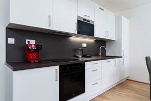 A modern kitchen with white cabinets, a black countertop, a red coffee machine, a kettle, and an oven.