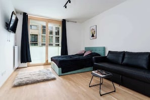 A modern bedroom with a bed, a black leather sofa, a small table, and a view of the outside through a sliding door.