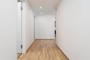 A narrow hallway with wooden flooring and white walls.