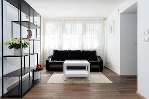 Un salon moderne avec un canapé noir, une table basse blanche et une étagère noire agrémentée de fleurs.