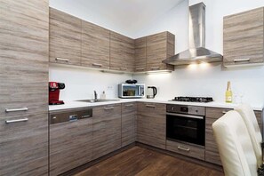 A modern kitchen with wood-textured cabinets, stainless steel appliances, and a built-in microwave. - Deluxe Rabbit Suite (Prague 2)