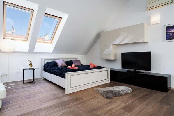 A bedroom with a bed, a TV, a desk, and a window.