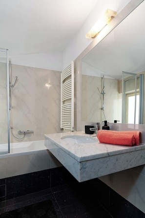 A modern bathroom with a marble vanity, a glass shower enclosure, and a large mirror.