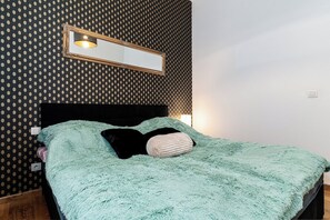 Una cama con una manta verde mullida, un cabecero negro y un espejo fijado a la pared con una lámpara encima.