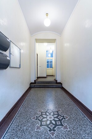 A hallway with a patterned floor, a door at the end, and a light fixture on the ceiling.