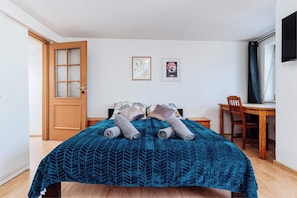 Um quarto com cama, porta de madeira, escrivaninha e cadeira.