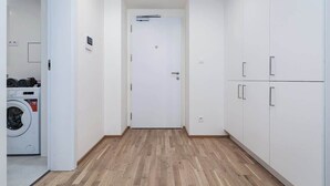 Un pasillo con lavadora, armarios blancos y una puerta con manija.