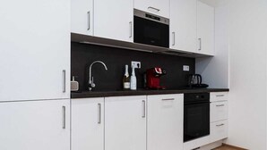 Una cocina moderna con armarios blancos, encimera negra, horno empotrado, cafetera y una botella de vino.