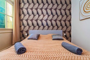 A neatly made bed with a patterned bedspread, two pillows, and rolled towels.