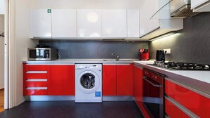 A modern kitchen with red and white cabinetry, a built-in washing machine, a microwave, a coffee maker, and a gas stove.