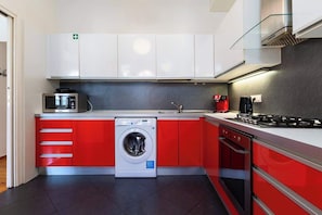 A modern kitchen with red and white cabinetry, a built-in washing machine, a microwave, a coffee maker, and a gas stove. - Big Cat Residence (Prague 2)