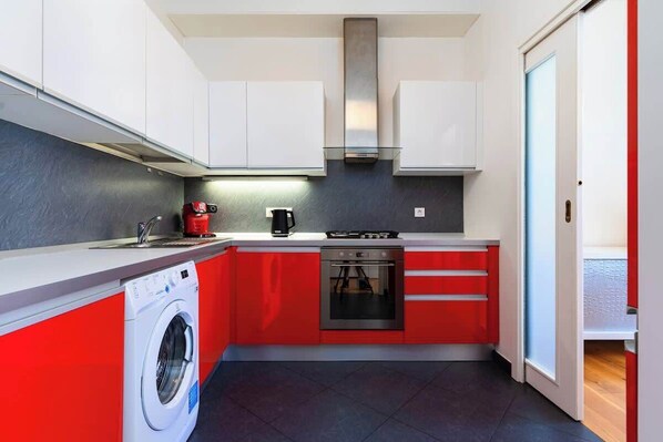 A compact kitchen with a washing machine, a coffee maker, and a stove.