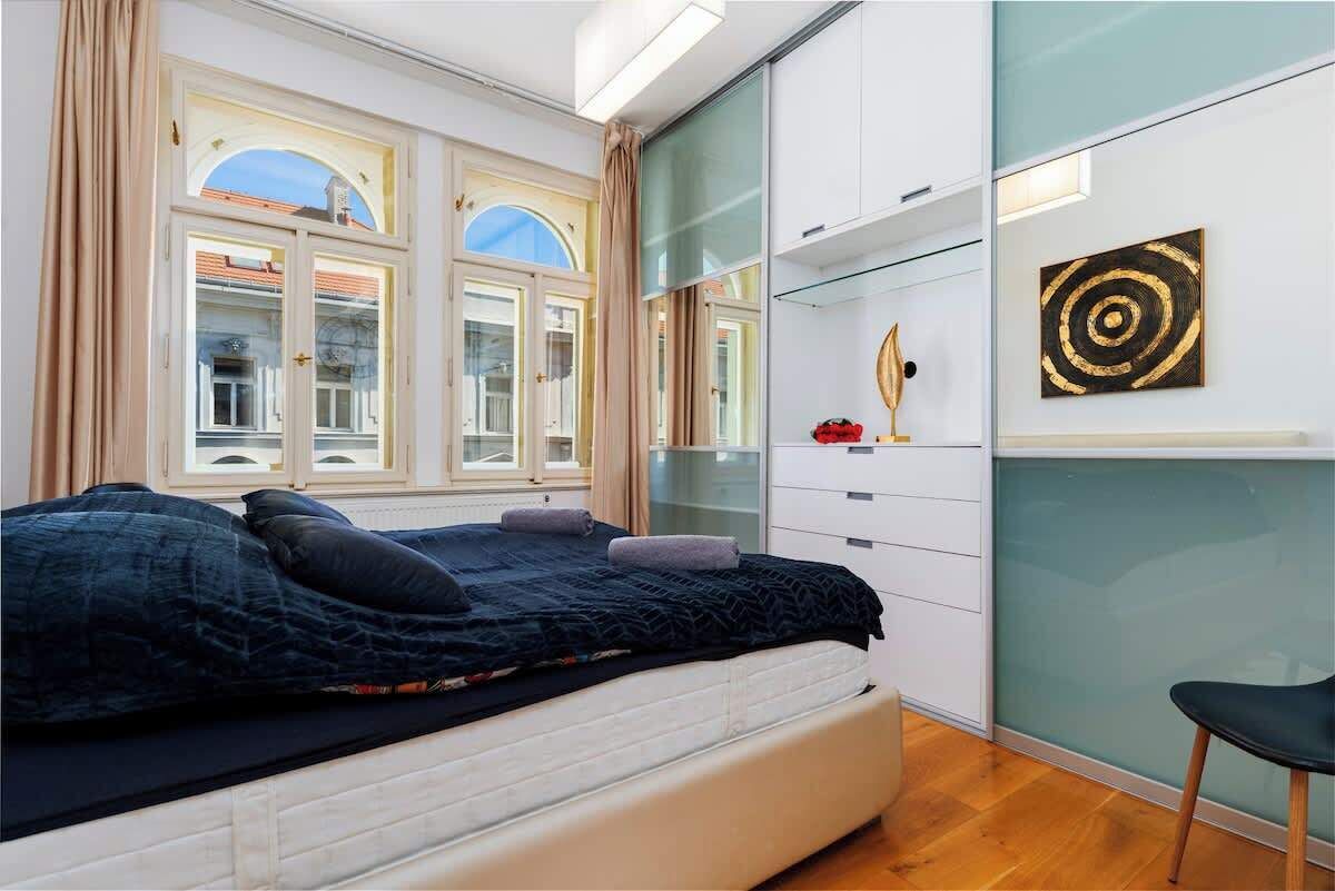 A bedroom with a bed, a wardrobe, a mirror, and a window with curtains.