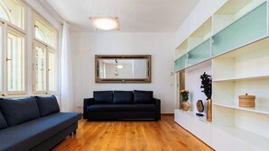 A modern living room with a dark sofa, wooden flooring, a large mirror, and a white shelving unit with decorative items.