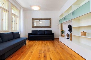 A modern living room with a dark sofa, wooden flooring, a large mirror, and a white shelving unit with decorative items. - Big Cat Residence (Prague 2)