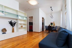 A modern living room with a blue sofa, wooden flooring, and a glass-fronted shelving unit.