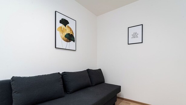 A modern living room with a dark grey sofa, two framed artworks on the wall, and a wooden floor. - Bohemian Deluxe Suite (Prague 5)