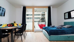 A modern bedroom with a bed, a dining table with chairs, a hanging chair, and a view of a building through a glass door. - Bohemian Deluxe Suite (Prague 5)