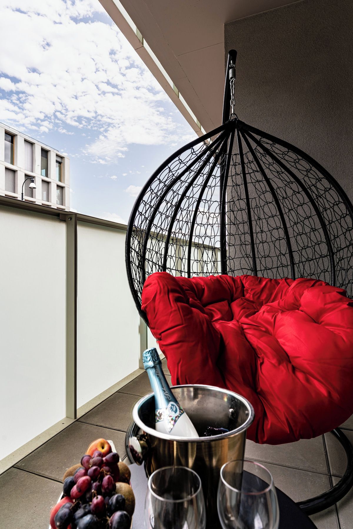 Ein Balkon mit einer Hängematte, einer Champagnerflasche und einer Obstschale.