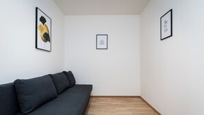 A minimalist room with a dark grey sofa, wooden flooring, and three framed artworks on the walls. - Bohemian Deluxe Suite (Prague 5)