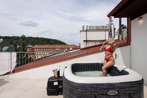 Uma pessoa de fato de banho vermelho sentada numa banheira insuflável numa varanda com vista para a cidade.
