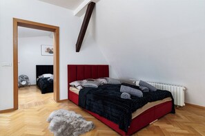 A bedroom with a red bed, a wooden floor, a white radiator, and a door leading to another room.
