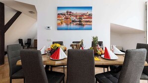 A dining area with a wooden table set for four, surrounded by grey upholstered chairs. A painting of a cityscape is mounted on the wall above the table.