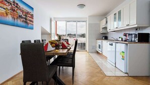 A modern kitchen with white cabinets, a dining area with a table and chairs, and a large window offering a view of the cityscape. - Royal Skyline Residence (Prague 5)