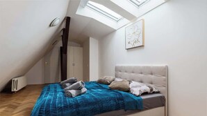 A bedroom with a sloped ceiling, a bed with a blue blanket, and a skylight. - Royal Skyline Residence (Prague 5)