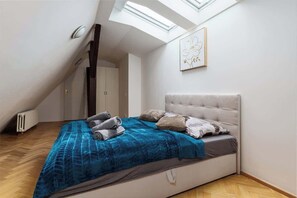 A bedroom with a sloped ceiling, a bed with a blue blanket, and a skylight. - Royal Skyline Residence (Prague 5)