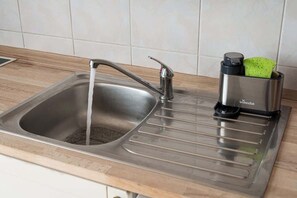 A stainless steel kitchen sink with a modern faucet and a container holding a green sponge.