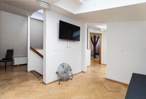 A spacious living area with a flat-screen TV mounted on the wall, a standing fan, and a wooden floor. - Royal Skyline Residence (Prague 5)