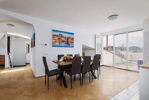 Un coin repas avec une table et des chaises en bois, un tableau représentant un paysage urbain accroché au mur et une grande fenêtre offrant une vue sur la ville.