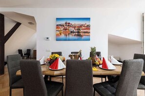 A dining area with a wooden table set for four, surrounded by grey upholstered chairs. A painting of a cityscape is mounted on the wall above the table. - Royal Skyline Residence (Prague 5)