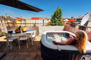 Una terraza en la azotea con jacuzzi, mobiliario exterior y vistas de la ciudad.