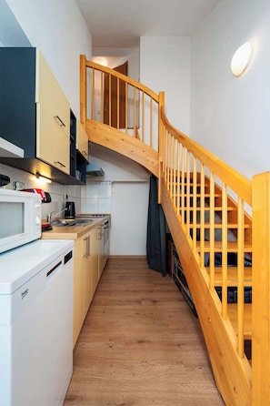 Cocina compacta con escalera de madera, armarios blancos y microondas.
