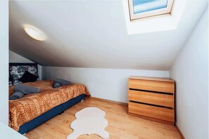 A bedroom with a bed, a wooden dresser, a small rug, and a skylight.