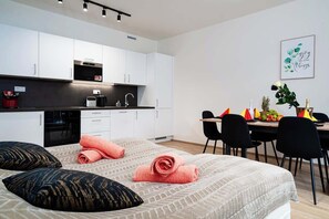 A modern hotel room with a bed, a small kitchenette, a dining area, and a wall with a framed quote.