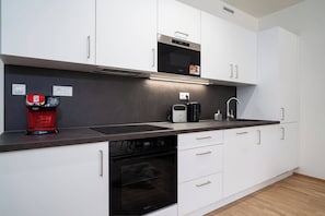 A modern kitchen with white cabinets, a black oven, a coffee machine, and a microwave.