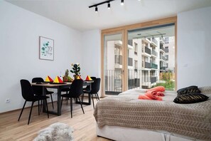 A modern bedroom with a bed, a dining table with chairs, and a view of the outside balcony.