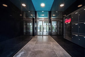 A modern lobby with a glass door entrance, a tiled floor, and a ceiling with recessed lighting.