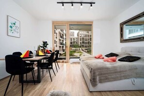 A modern bedroom with a bed, a dining table with chairs, a large window, and a view of buildings.
