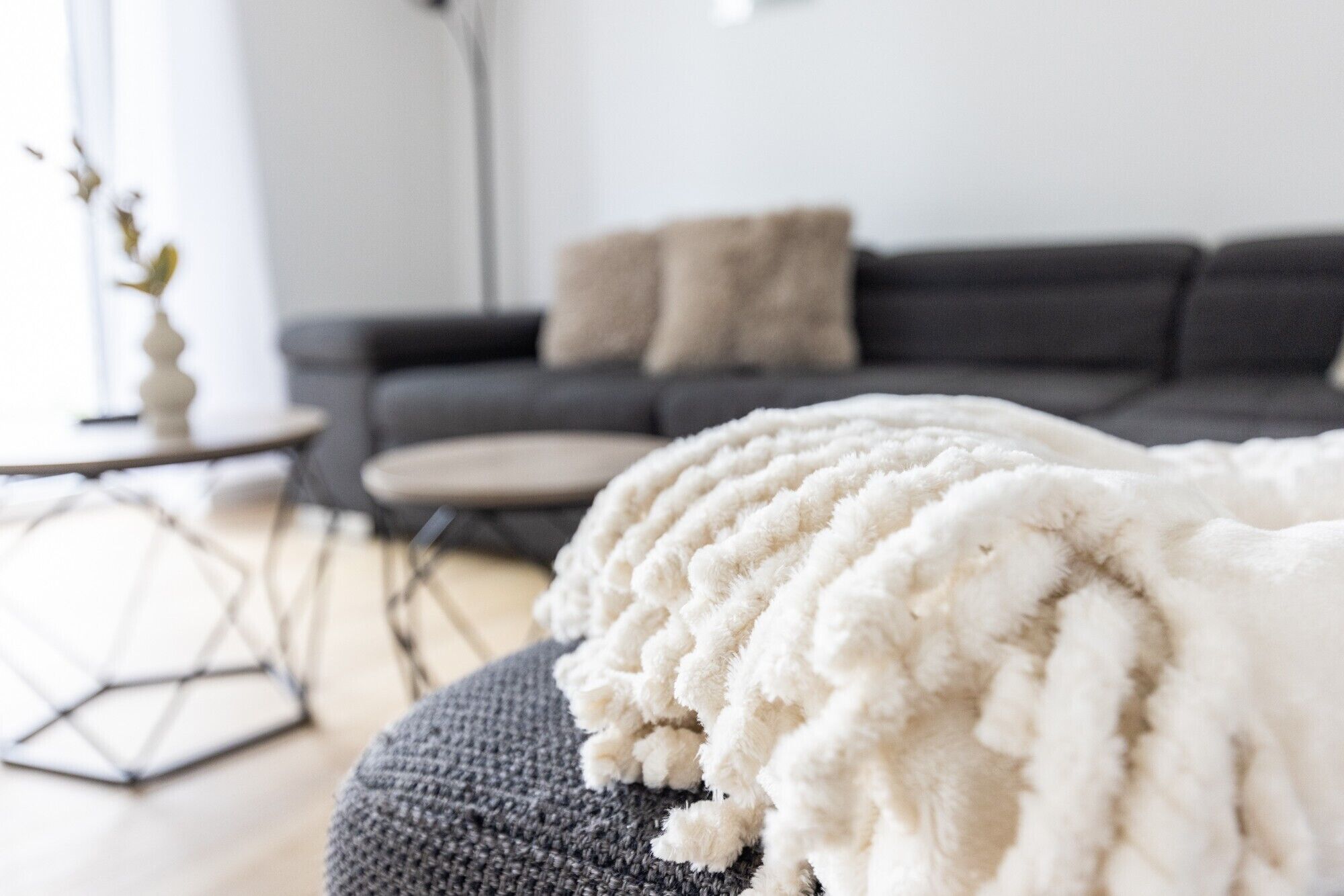 A living room with a grey sofa, a white throw blanket, and a small round table with a vase.