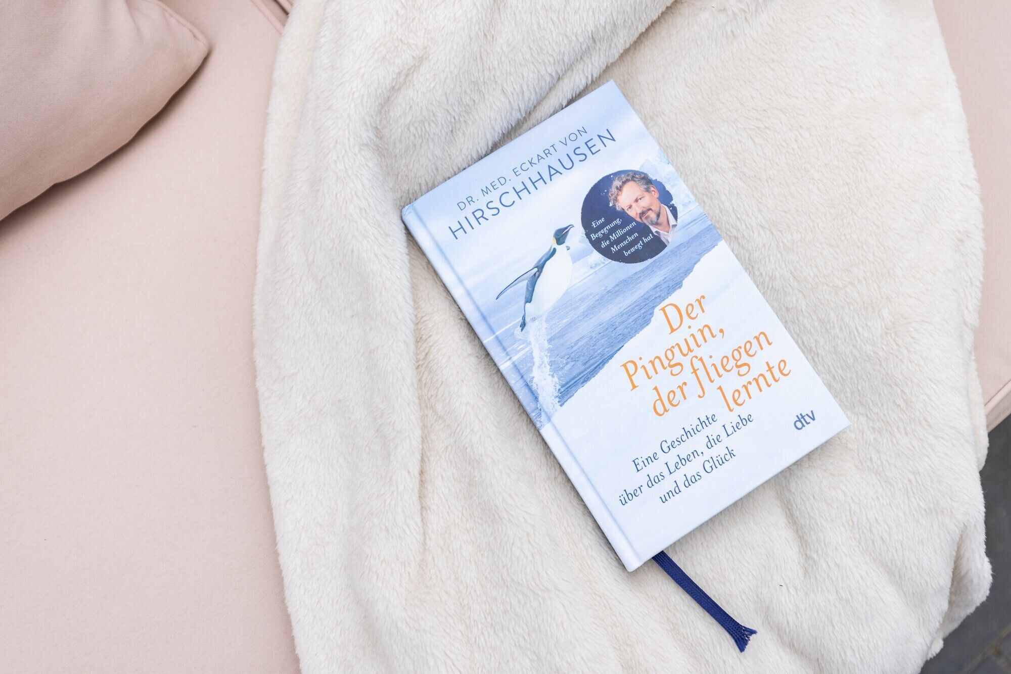 Un libro titulado 'Der Pinguin, der fliegt' del Dr. med. Eckart von HIRSCHHAUSEN, sobre una superficie blanca y mullida.