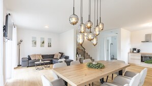 A modern living room with a wooden dining table, grey sofa, and a staircase leading to another level. - Holiday Home 'Das Strandhaus 2' with Shared Terrace and Wi-Fi (Lembruch)