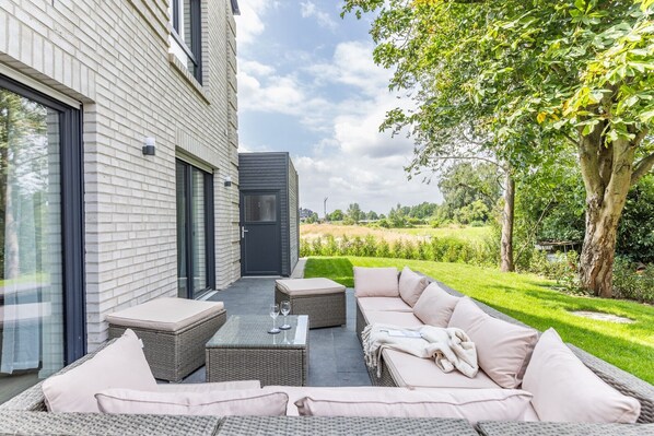 A patio with outdoor furniture, a glass door, and a view of a green landscape.