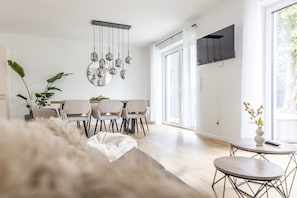 Un salon moderne avec un canapé, un coin repas avec des chaises, une table basse et une grande fenêtre avec des rideaux.