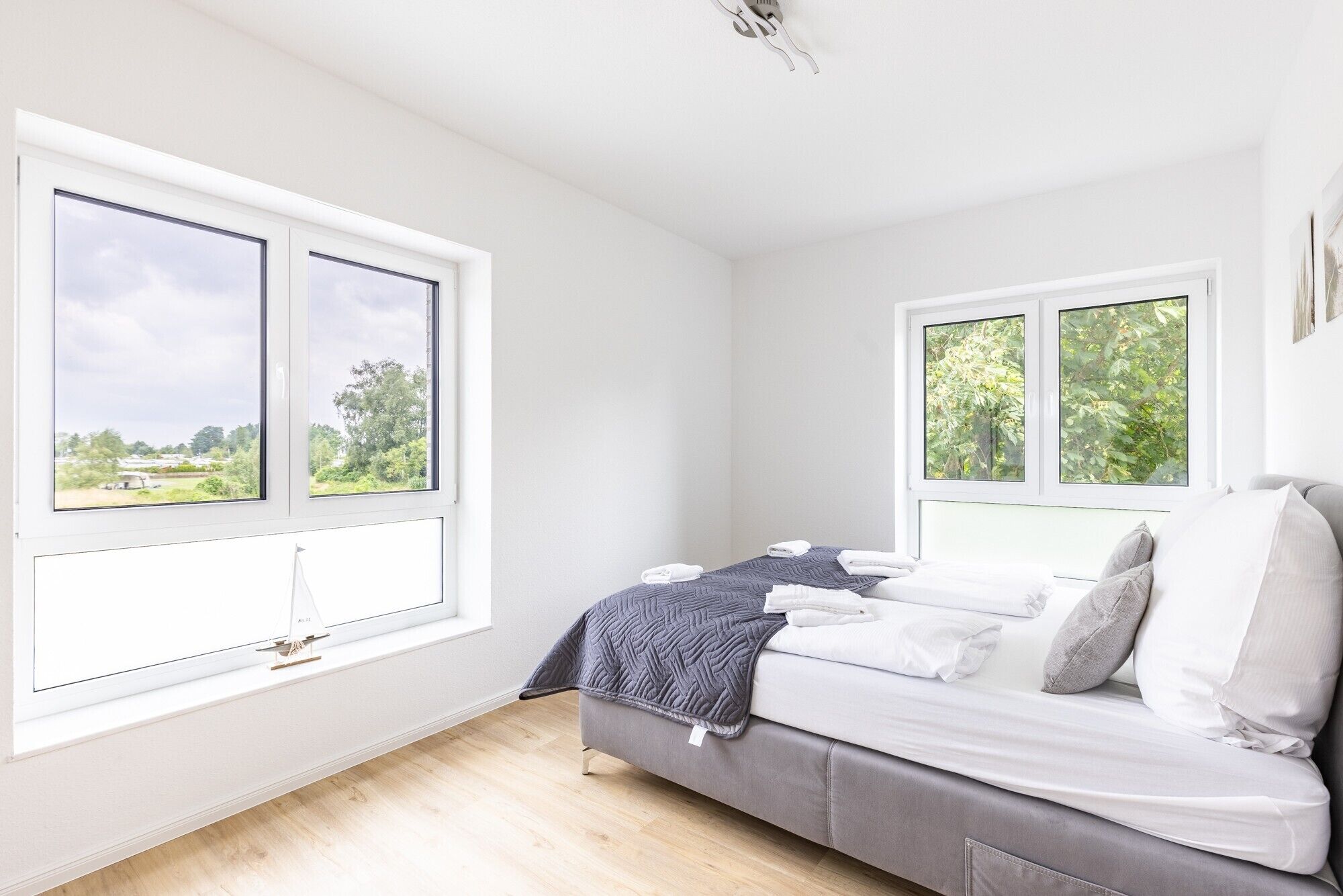 Een slaapkamer met twee grote ramen, een bed met witte lakens en een grijze bank.