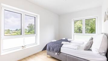 Een slaapkamer met twee grote ramen, een bed met witte lakens en een grijze bank.