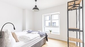 A minimalist bedroom with a bed, bedside lamp, window, and a metal rack. - Holiday Home 'Das Strandhaus 2' with Shared Terrace and Wi-Fi (Lembruch)